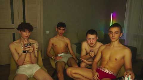 Media: Video of four shirtless young men in white and red Calvin Klein underwear, sitting casually in a dimly lit room with wooden furniture and colorful neon lights.