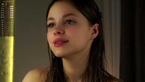 Media: A video of a young, light-skinned woman with wet, dark brown hair and a slight smile, standing in front of a shower.