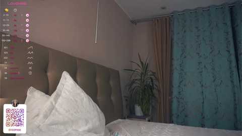 Media: A video of a modern bedroom with a bed featuring white pillows and a tufted headboard. The room has teal curtains and a green potted plant. A smartphone screen with a QR code is visible.