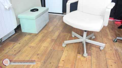 Media: A video of a modern office chair with a white leather seat and frame on a wooden floor. To the left, a light blue storage box and white cabinet are visible.