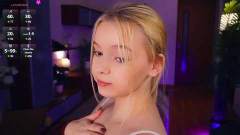 Media: Video of a blonde, fair-skinned woman with a slender physique, wearing a white tank top, indoors with dim lighting, modern decor, and a \"Live\" status on a screen.