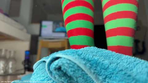 Media: Video of colorful, striped Christmas socks and a turquoise towel on a white counter, blurred background with kitchen items and a television.