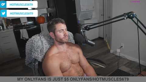 Media: Video of a shirtless, muscular, light-skinned man with short brown hair, seated in a chair, with a microphone in front of him. Kitchen in the background. Text overlay reads: \"My OnlyFans is just $5 onlyfanshotmuscle69.\