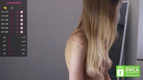 Media: Video of a topless, light-skinned woman with long, straight, blonde hair, partially obscured. Background includes a grey wall and a window frame. The image includes a \"DMPA Shielded\" watermark.