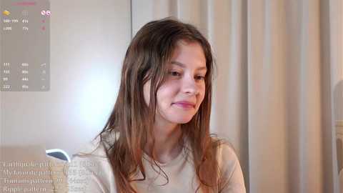 Media: Video of a young girl with long, wet hair, wearing a beige top, in a bathroom with a digital thermometer display and white curtains.