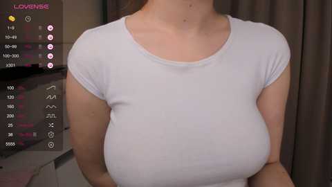 Media: Video of a fair-skinned woman with large breasts, wearing a snug white T-shirt, taken indoors with a digital screen overlay displaying live streaming statistics.