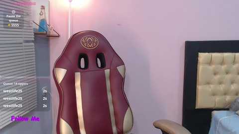 Media: Video of a modern gaming chair with maroon and gold accents, placed against a light purple wall, next to a tufted headboard and a window with closed blinds.