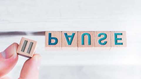 Media: Video of a hand holding a wooden block with the word \"BUNZE\" in turquoise letters. The background is a blurred white wall. The hand is Caucasian, with clean-cut nails. The wooden block is light brown with a smooth texture.