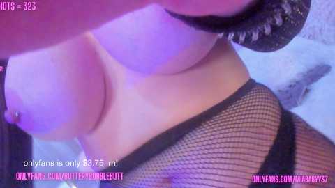 Media: A close-up video of a light-skinned woman's bare breasts, with nipples pierced and covered in black fishnet stockings, taken in a dimly lit room with purple lighting. The image includes text at the bottom left and right corners, promoting OnlyFans and TitsBurgundy.