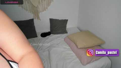 Media: A video of a woman lying on a bed with white sheets, gray pillows, and a beige pillow, surrounded by minimalistic decor.