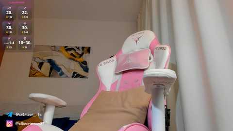 Media: Video of a pink and white gaming chair with a cushioned headrest, placed in a dimly lit room with a colorful abstract painting on the wall.