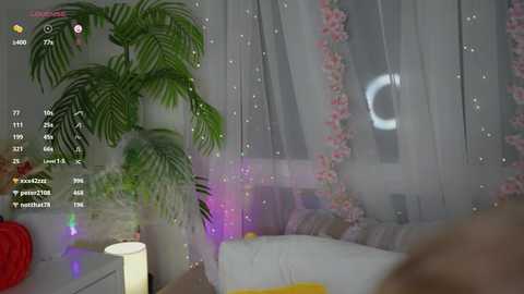 Media: A dimly lit room with a large potted plant, a white couch, pink flower garland, and a glowing lunar crescent moon through sheer curtains.