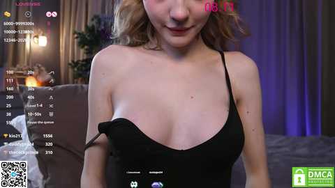 Media: Video of a fair-skinned woman with blonde hair, wearing a black spaghetti-strap dress, captured in a dimly-lit room with a TV displaying a webcam feed and a \"DMCA NOTICE\" watermark.