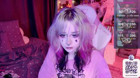 Media: Video of a young woman with messy, platinum blonde hair, dark roots, and purple highlights, wearing a white T-shirt with a skull design, sitting in a dimly lit bedroom with a bed covered in floral sheets.