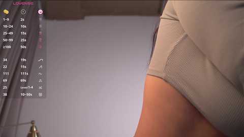 Media: Video of a close-up of a woman's lower torso in beige shorts, with a virtual overlay showing a fitness app. Background includes a white wall and part of a bed.