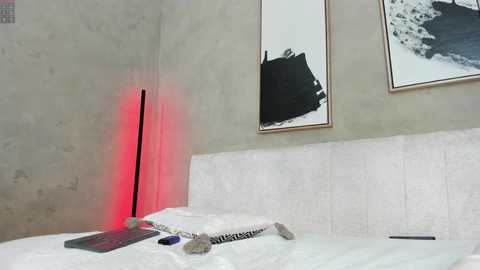 Media: Video of a minimalist bedroom with white bed, minimalist art on beige walls, and a red-lit standing lamp in the corner.