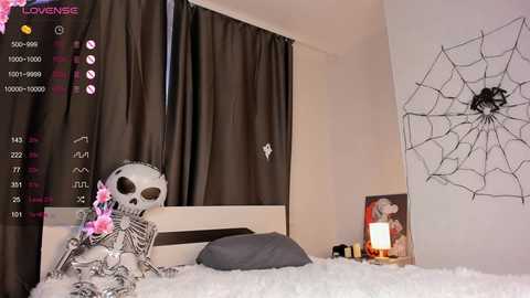 Media: Video of a bedroom with a skeleton doll on a bed, surrounded by dark curtains, a spiderweb drawing, and a nightstand with a lamp.