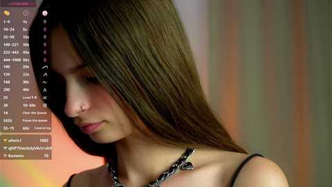 Media: Video of a young woman with long, straight brown hair, wearing a black top and chain necklace. Background features a blurred, colorful gradient.