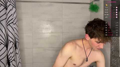 Media: A video shows a shirtless young man with wet hair, wearing a black necklace, in a shower with white tiled walls and a black-and-white patterned curtain.