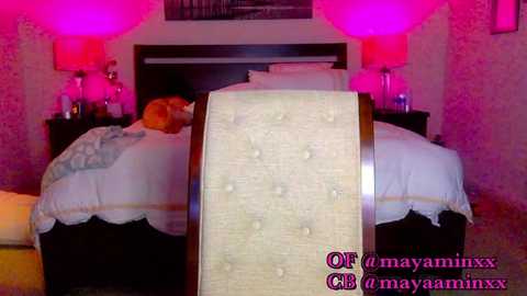 Media: Video of a pink-lit bedroom with a tufted headboard, white bedspread, and two bedside lamps.