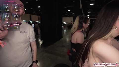 Media: Video of a dimly lit, crowded room with a man in a beige shirt, a woman in a black top, and others in the background.