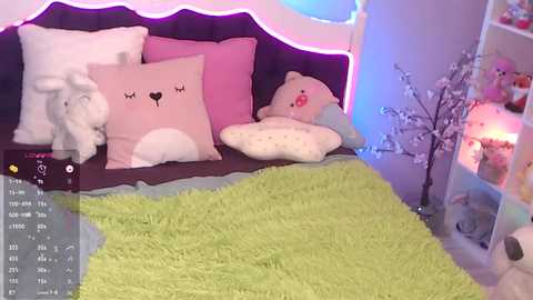 Media: Video of a cozy bedroom with a plush white elephant toy, pastel pillows, and a green shaggy rug, lit by soft purple and blue LED lights, with a virtual reality headset screen on the left.