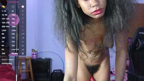 Media: Video of a nude, light-skinned, transgender woman with long black hair, wearing red lipstick, in a bedroom with a black chair and a desk.