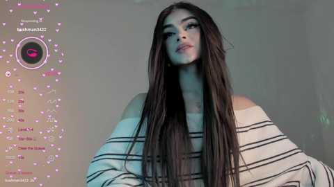 Media: Video of a young woman with long, straight, dark hair, wearing a striped off-the-shoulder sweater. The background is a blurred, muted gray. Overlay shows social media metrics and a pink heart icon.