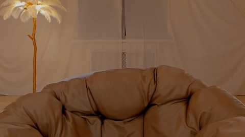 Media: A video of a cozy, beige leather recliner chair in a dimly lit room, with a large, white feather lamp in the background and sheer white curtains draped around the window.