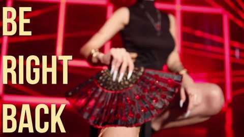 Media: A video of a woman in a black sleeveless top and a red sequined skirt with gold accents, posing against a red geometric background. Bold yellow text reads \"BE RIGHT BACK.\