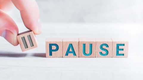 Media: Video of a person's hand holding a wooden block with the letter \"P\" on it. The block is part of a word puzzle spelling \"PAUSE,\" which is made up of wooden blocks with blue letters. The background is a plain, light-colored surface.