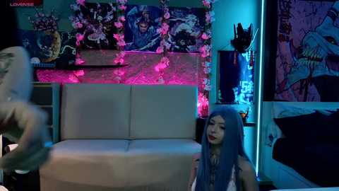 Media: Video of a dimly lit room with a white couch, pink and blue neon lights, and a young Asian woman with long blue hair, sitting on the floor.