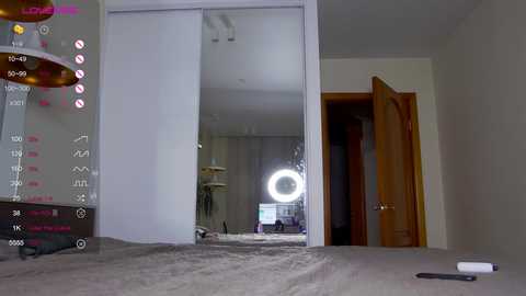 Media: Video of a modern bedroom with a large mirror, a bed, a wooden door, and a ring light.