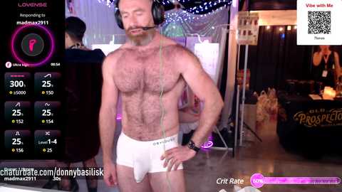 Media: Video of a bearded, muscular, white man in white underwear, wearing headphones, standing in a dimly lit room with a live stream overlay.