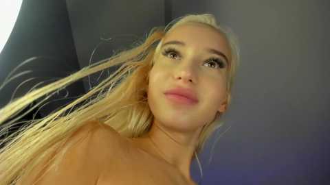 Media: Video of a blonde woman with light skin, looking up with parted lips, slightly tousled hair, and visible collarbone.