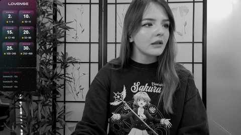 Media: A black-and-white video of a young woman with long hair, wearing a \"Sailor Moon\" t-shirt, standing indoors against a shoji screen.