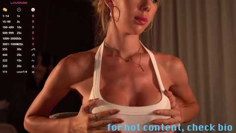 Media: A video of a slender, light-skinned woman with large breasts wearing a white halter top, her hands pressing down on her chest. The background is dimly lit with a video game overlay and text reading \"for hot content, check big.\