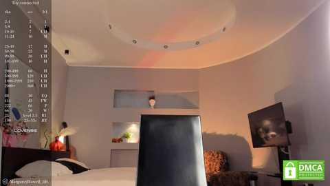 Media: Video of a modern bedroom with a large flat-screen TV, minimalistic decor, recessed lighting, and a cozy corner with a cushioned chair.