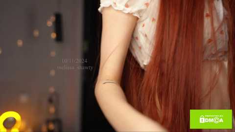 Media: Video of a young woman with long, straight, reddish-brown hair, wearing a floral-patterned top, bending her right arm, showcasing a thin, silver bracelet. Background features a blurred, softly lit room with a green \"Euronews\" logo in the bottom right corner.