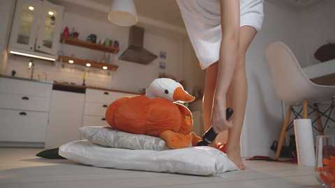 Media: Video of a person in a white robe and slippers, standing on a cushioned platform with an orange duck toy, in a modern, white kitchen with stainless steel appliances and wooden shelves.