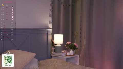 Media: A video of a dimly lit bedroom featuring a bed with a beige blanket, a white nightstand with a lamp, and pink roses.