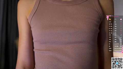 Media: Video of a woman's torso in a fitted, ribbed, light brown sleeveless top, showcasing her slim physique. The background features a dark curtain and a partially visible QR code.