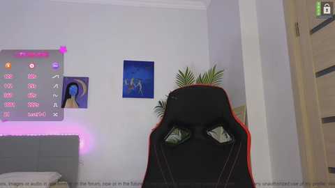 Media: Video of a gaming setup with a black and red gaming chair, a gray bed with purple LED lights, and a large blue poster on a white wall.