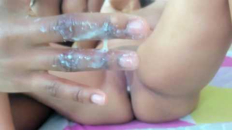 Media: A video shows a close-up of a person's hands and genitals, with semen on fingers and skin, and a colorful striped fabric in the background.