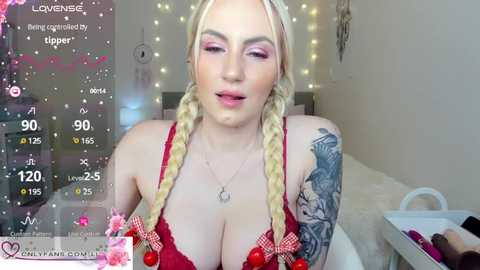 Media: Video of a blonde woman with pink eyeshadow, wearing a red bra, in a room with fairy lights and a white chair.