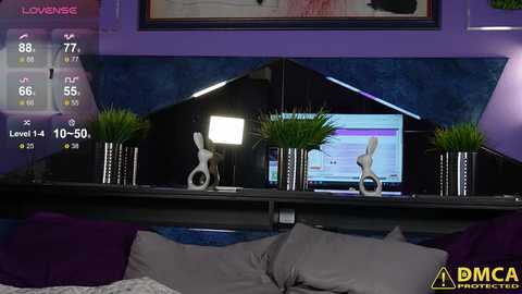 Media: Video of a modern bedroom with purple walls, black furniture, and two white dog statues in vases on a mirrored shelf. A digital game screen and a bed with gray pillows are visible.