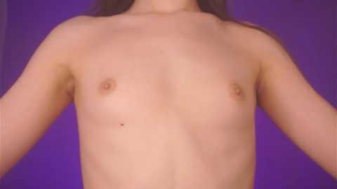 Media: Video of a young, light-skinned person with small breasts and dark nipples, standing against a solid purple background. The image is topless, focusing on the torso.