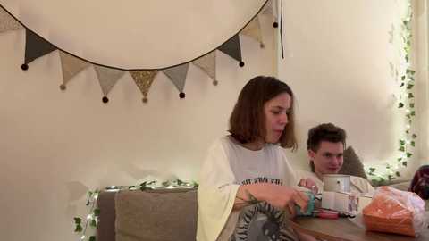 Media: Video of a woman and a man sitting at a table in a cozy room, adorned with string lights and bunting.