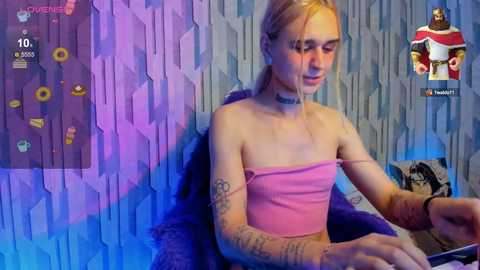 Media: Video of a slender, pale-skinned, blonde woman in a strapless pink crop top, with tattoos, sitting at a desk in a blue-lit room, surrounded by gaming UI elements and a \"Winston\" icon.