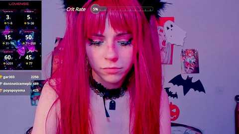 Media: Video of a pale-skinned, long-haired woman with vibrant pink hair and black cat ears, wearing a black choker, in a room with Halloween decorations.